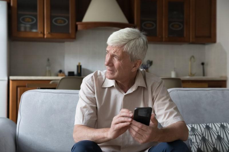 What’s That Smell Coming From My Furnace? Photo of a man on his phone looking out a window from his couch, seemingly worried.